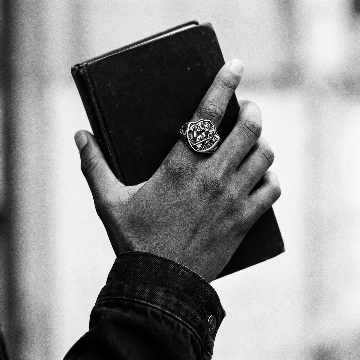 Black and white photo of a hand holding a black book wearing the Archangel Michael signet ring