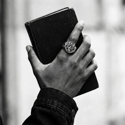 Black and white photo of a hand holding a black book wearing the Archangel Michael signet ring