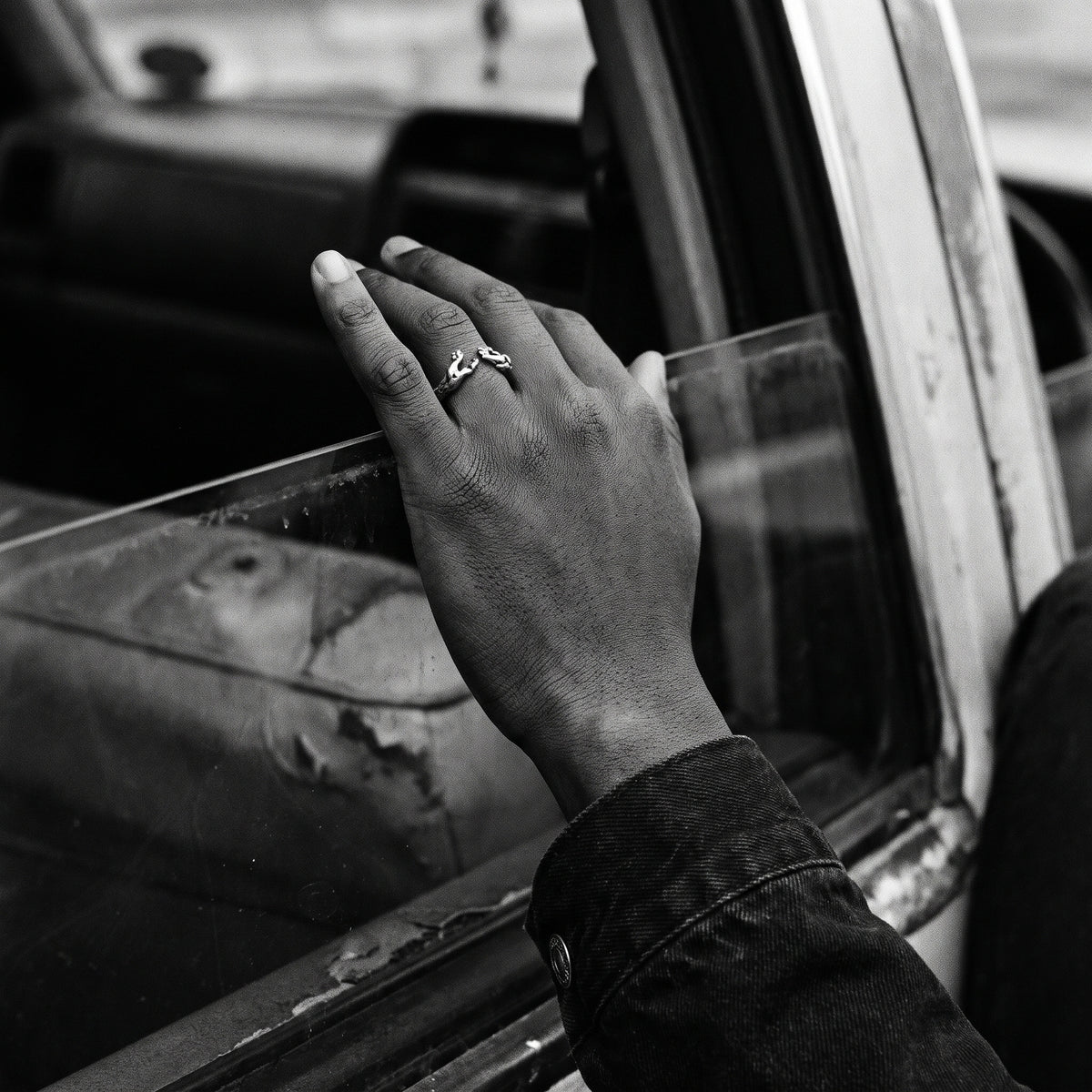 Man's hand on a car window sill wearing the Ascension hands of God ring, black and white film photo