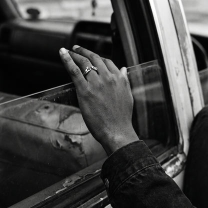 Man's hand on a car window sill wearing the Ascension hands of God ring, black and white film photo