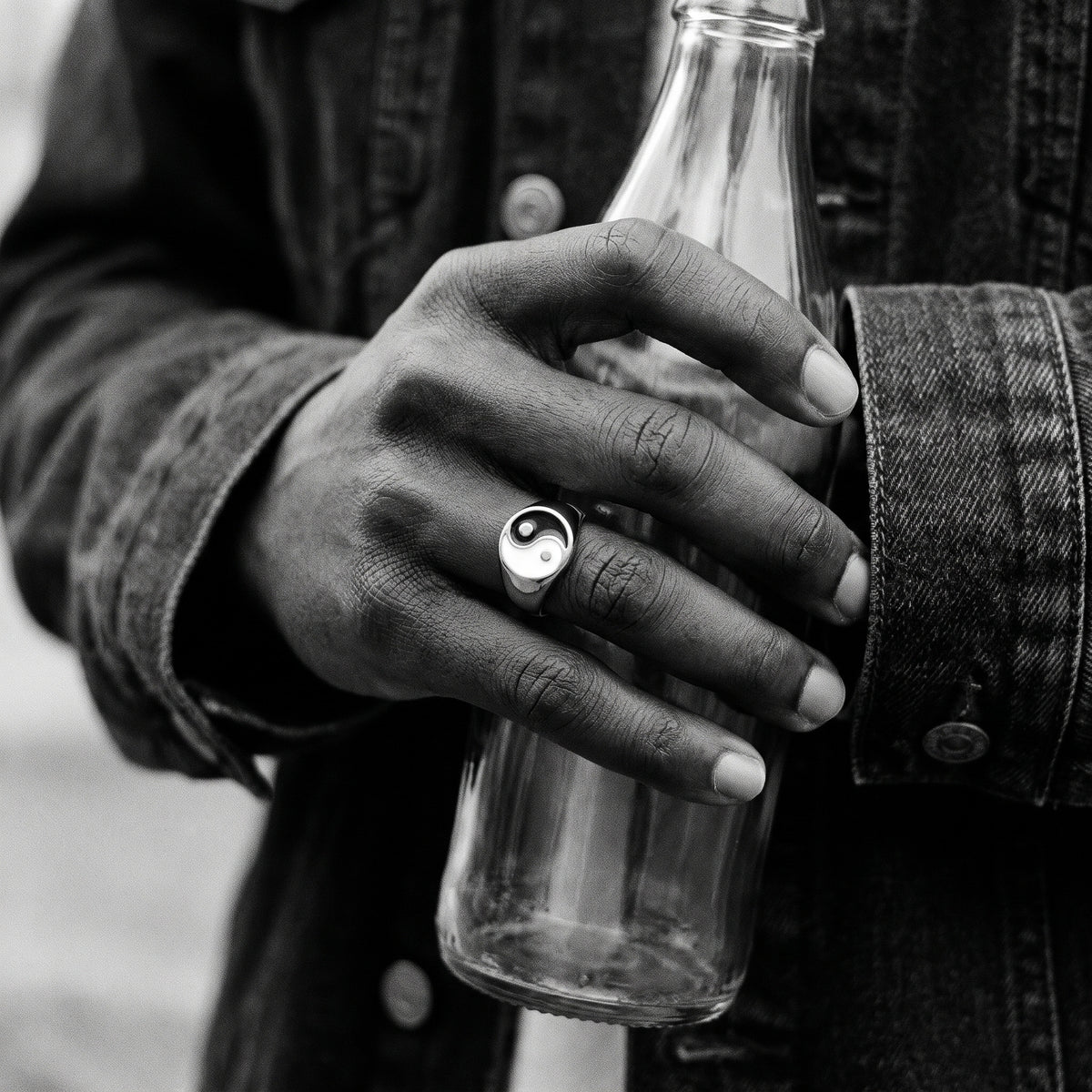 Black and white photo of a hand holding a glass bottle wearing the Eclipse yin-yang signet ring