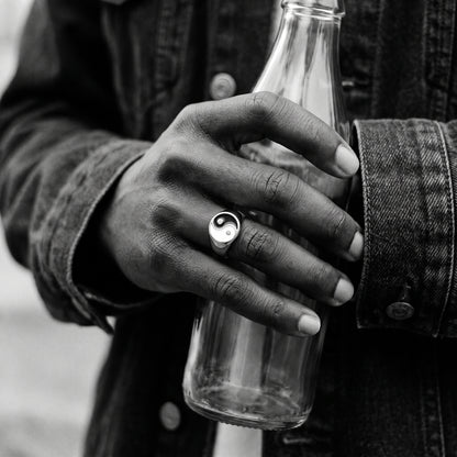 Black and white photo of a hand holding a glass bottle wearing the Eclipse yin-yang signet ring