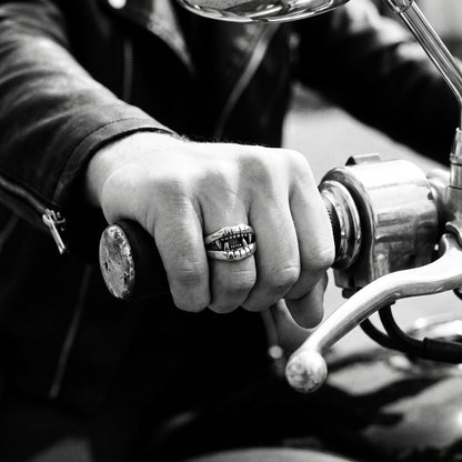 Young man's hand in a black leather jacket gripping a motorcycle handlebar, wearing the Fang devil mouth ring, black and white 35mm film