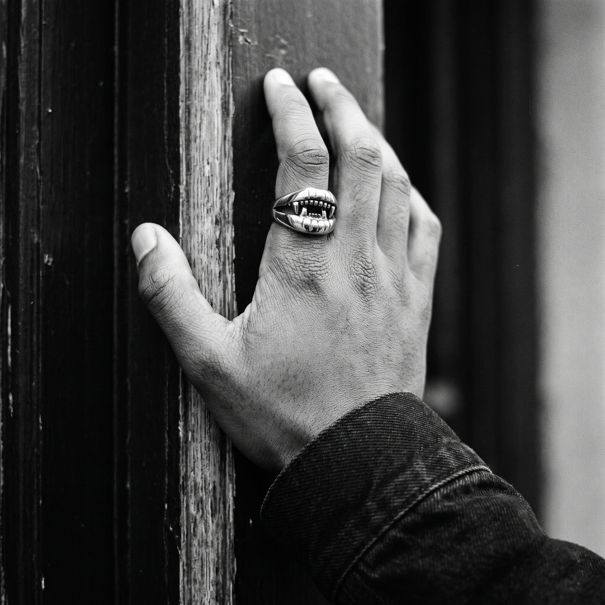 Man's hand on a doorframe wearing the Fang devil mouth ring, black and white film photo