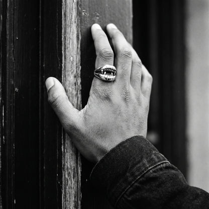 Man's hand on a doorframe wearing the Fang devil mouth ring, black and white film photo