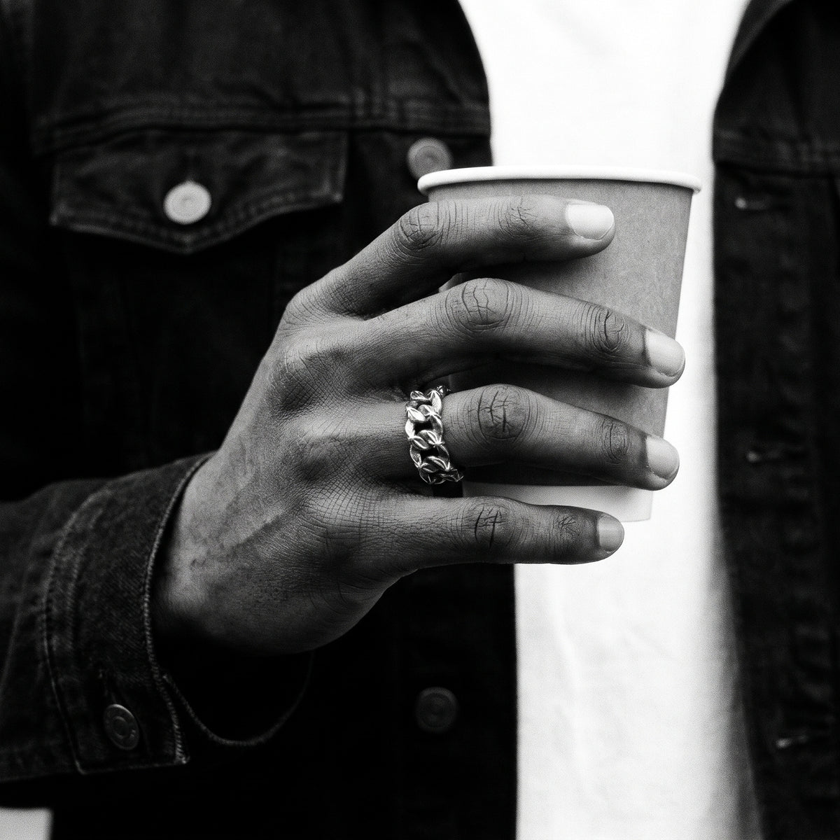 Black and white photo of a hand holding a paper coffee cup wearing the Havana Cuban link ring