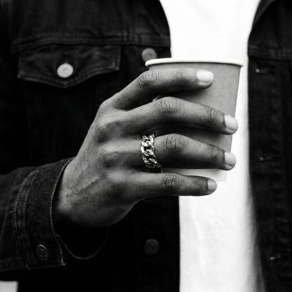 Black and white photo of a hand holding a paper coffee cup wearing the Havana Cuban link ring
