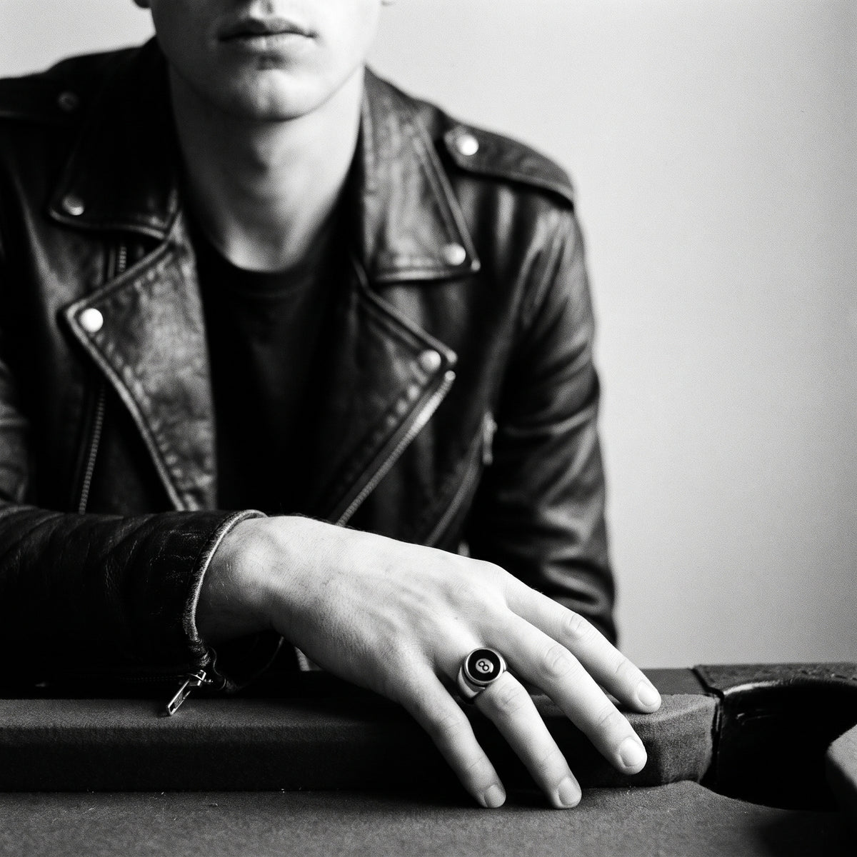 Young man's hand resting on a pool table edge in a black leather jacket, wearing the Hustler 8-ball ring, black and white 35mm film