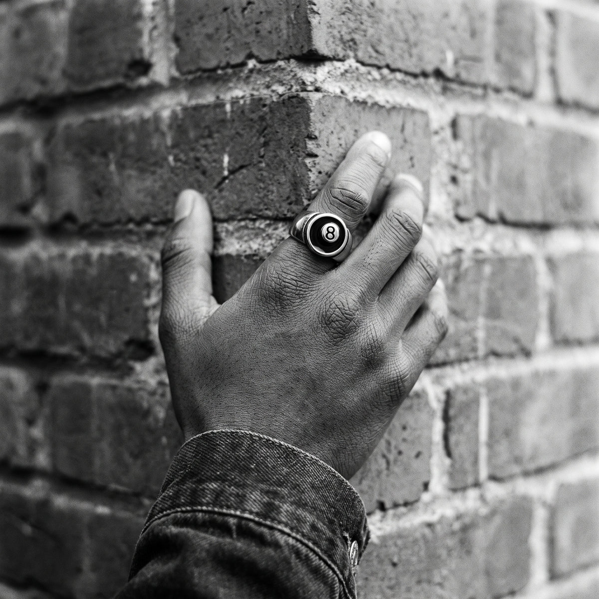 Man's hand on a brick corner wearing the Hustler 8-ball ring, black and white film photo