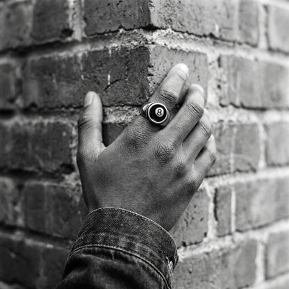 Man's hand on a brick corner wearing the Hustler 8-ball ring, black and white film photo