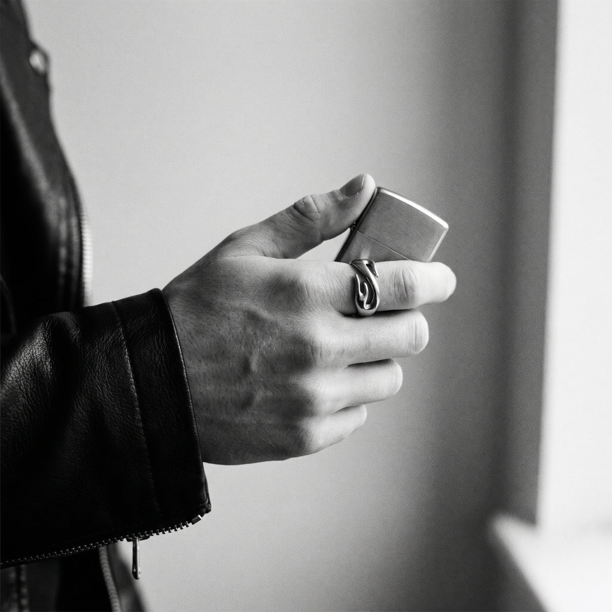 Black and white photo of a hand holding a closed lighter wearing the Inferno flame ring