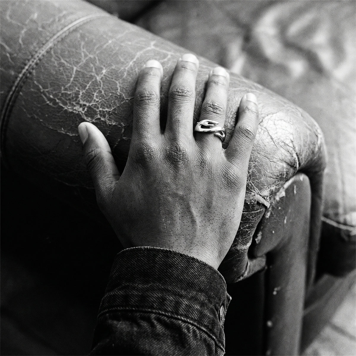 Black and white photo of a hand resting on a leather couch armrest wearing the Inferno flame ring