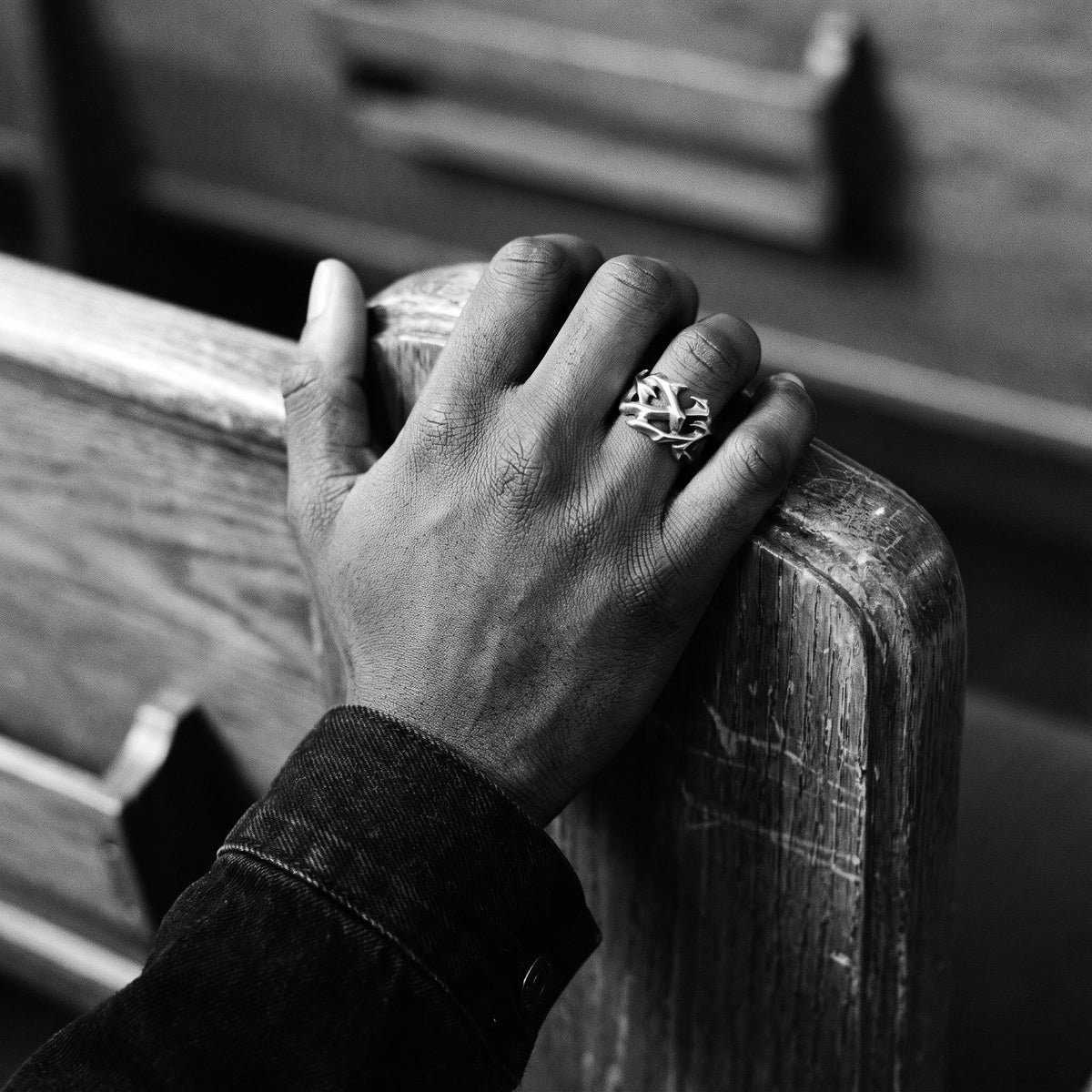 Black and white photo of a hand gripping a wooden church pew wearing the Penance crown of thorns ring
