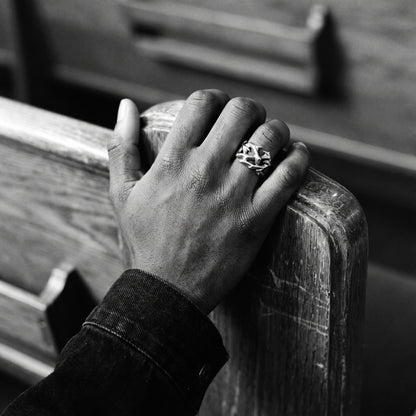 Black and white photo of a hand gripping a wooden church pew wearing the Penance crown of thorns ring
