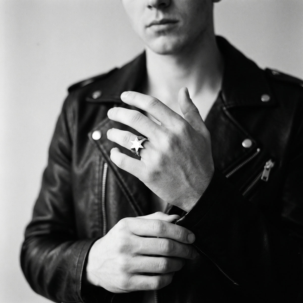 Young man's hand adjusting a black leather jacket cuff, wearing the Polaris six-point star ring, black and white 35mm film