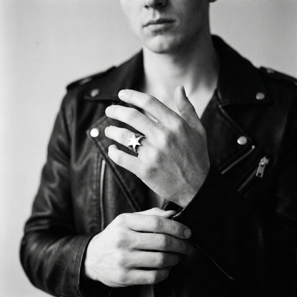 Young man's hand adjusting a black leather jacket cuff, wearing the Polaris six-point star ring, black and white 35mm film