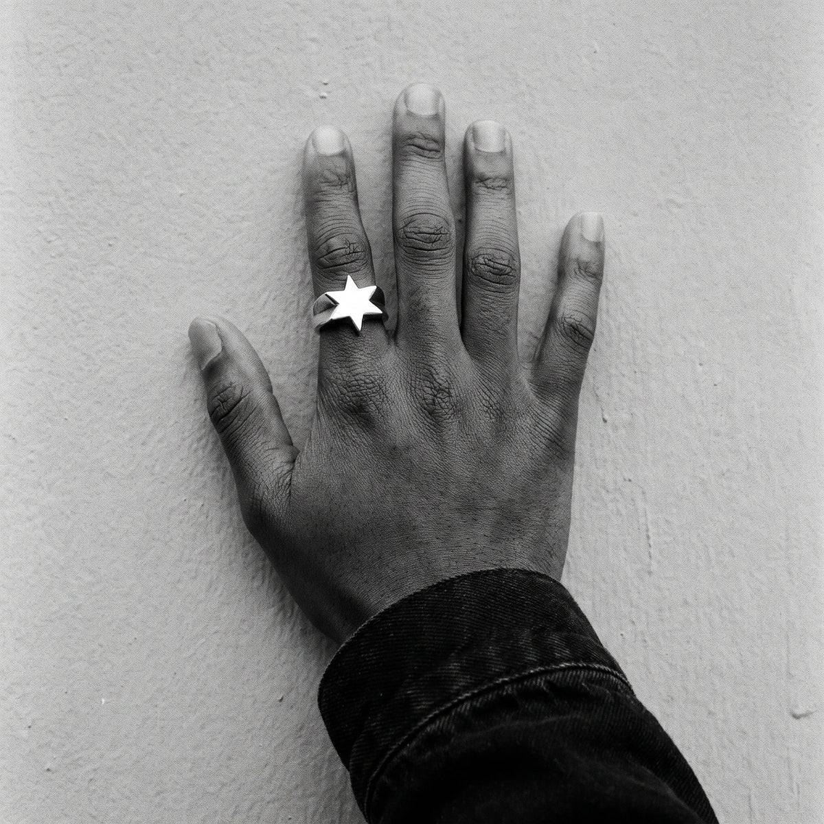 Man's hand on a wall wearing the Polaris six-point star ring, black and white film photo