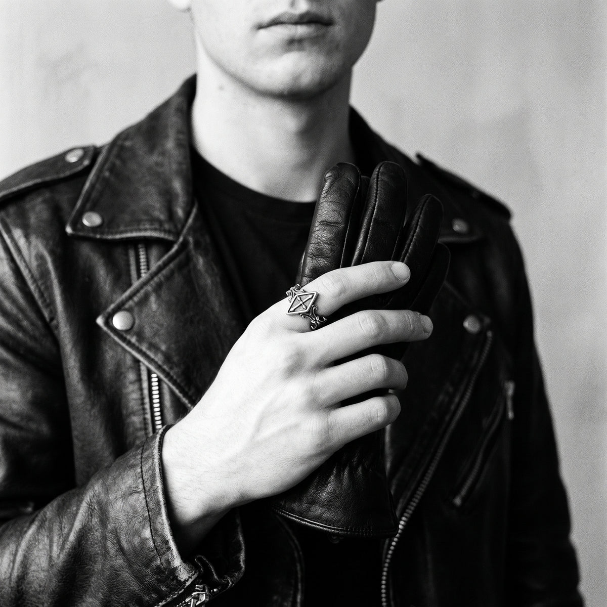 Black and white photo of a hand holding a leather glove wearing the Relic rhombus cross ring