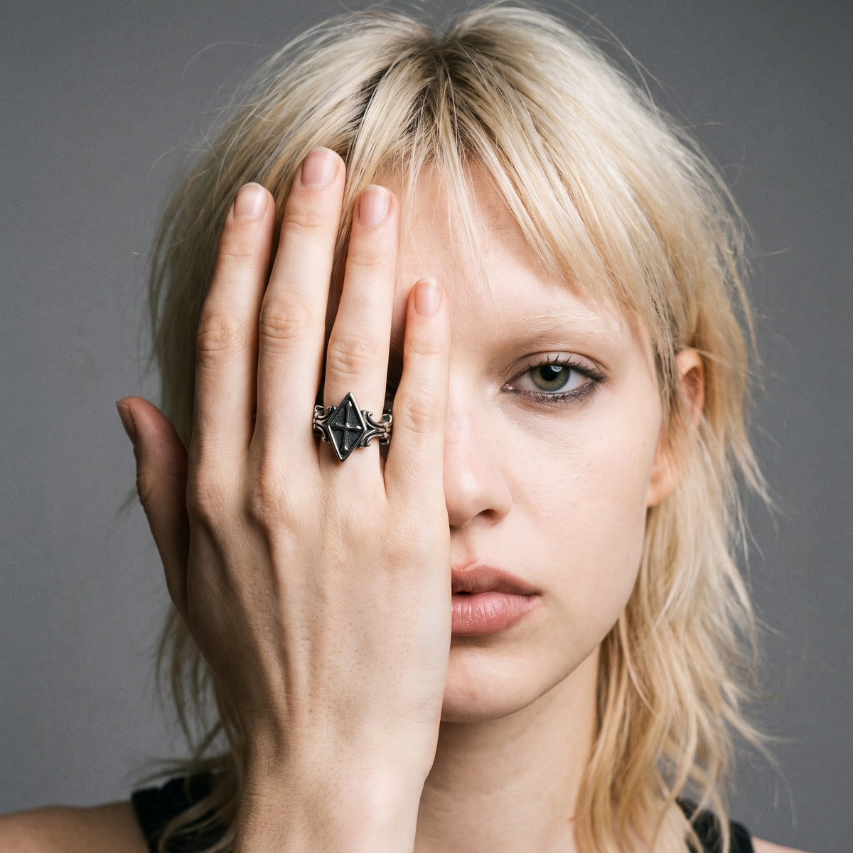 Blonde model with her hand over half her face wearing the Relic rhombus cross ring