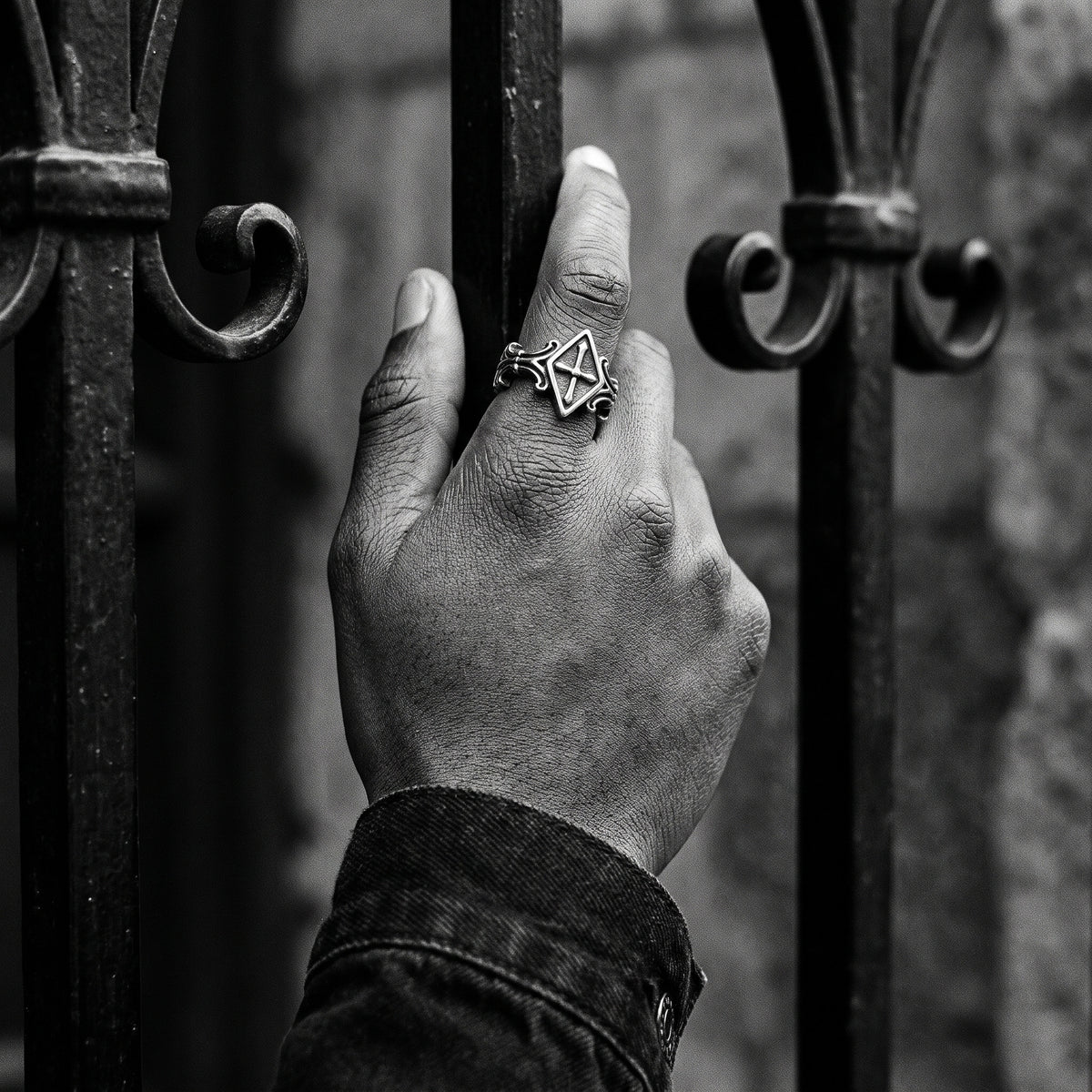 Black and white photo of a hand gripping a wrought-iron gate wearing the Relic rhombus cross ring