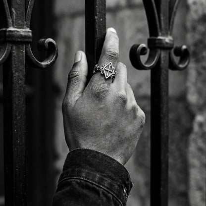 Black and white photo of a hand gripping a wrought-iron gate wearing the Relic rhombus cross ring
