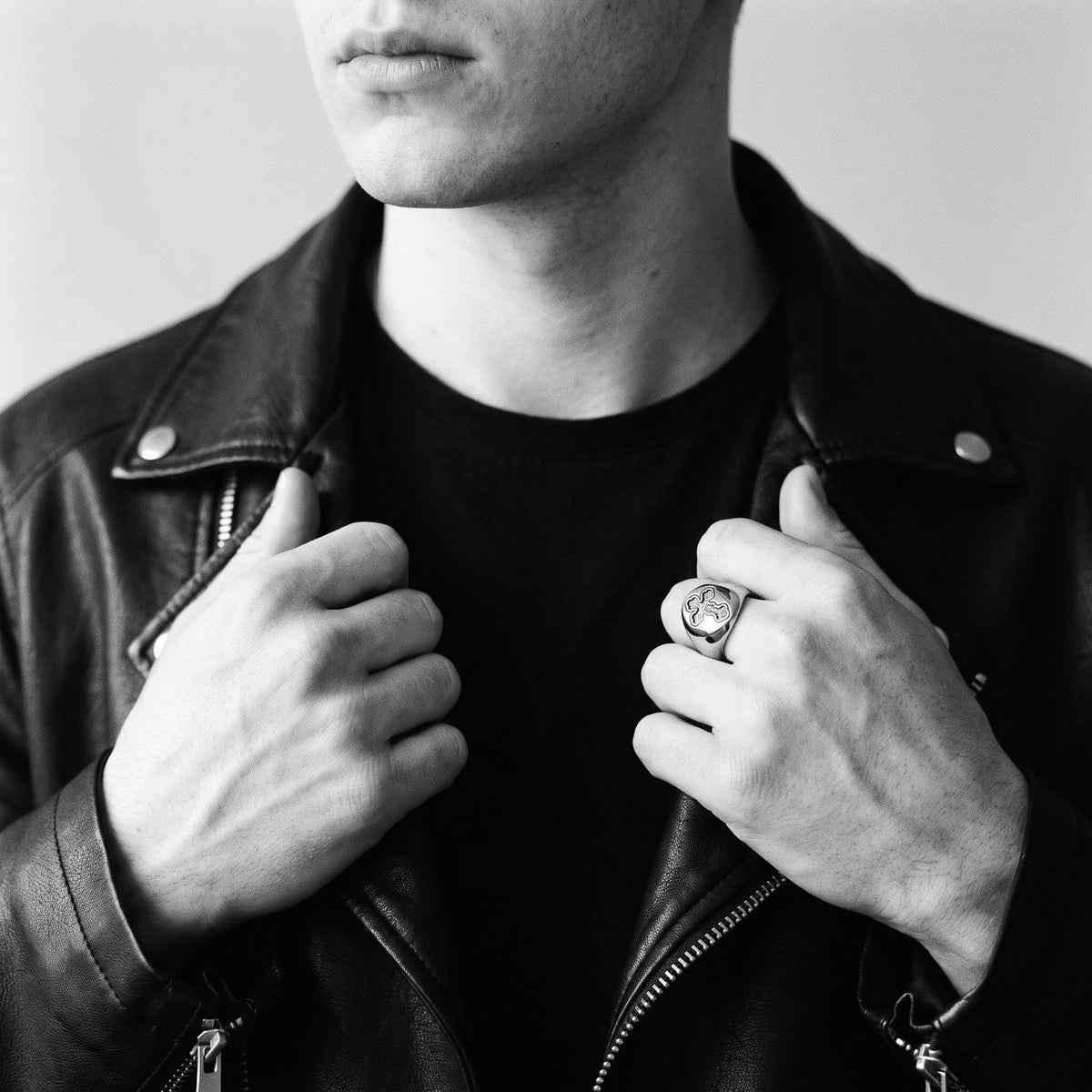 Black and white photo of a man in a black leather biker jacket gripping the lapels, wearing the Reliquary Cross Amulet Ring on his index finger