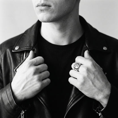 Black and white photo of a man in a black leather biker jacket gripping the lapels, wearing the Reliquary Cross Amulet Ring on his index finger