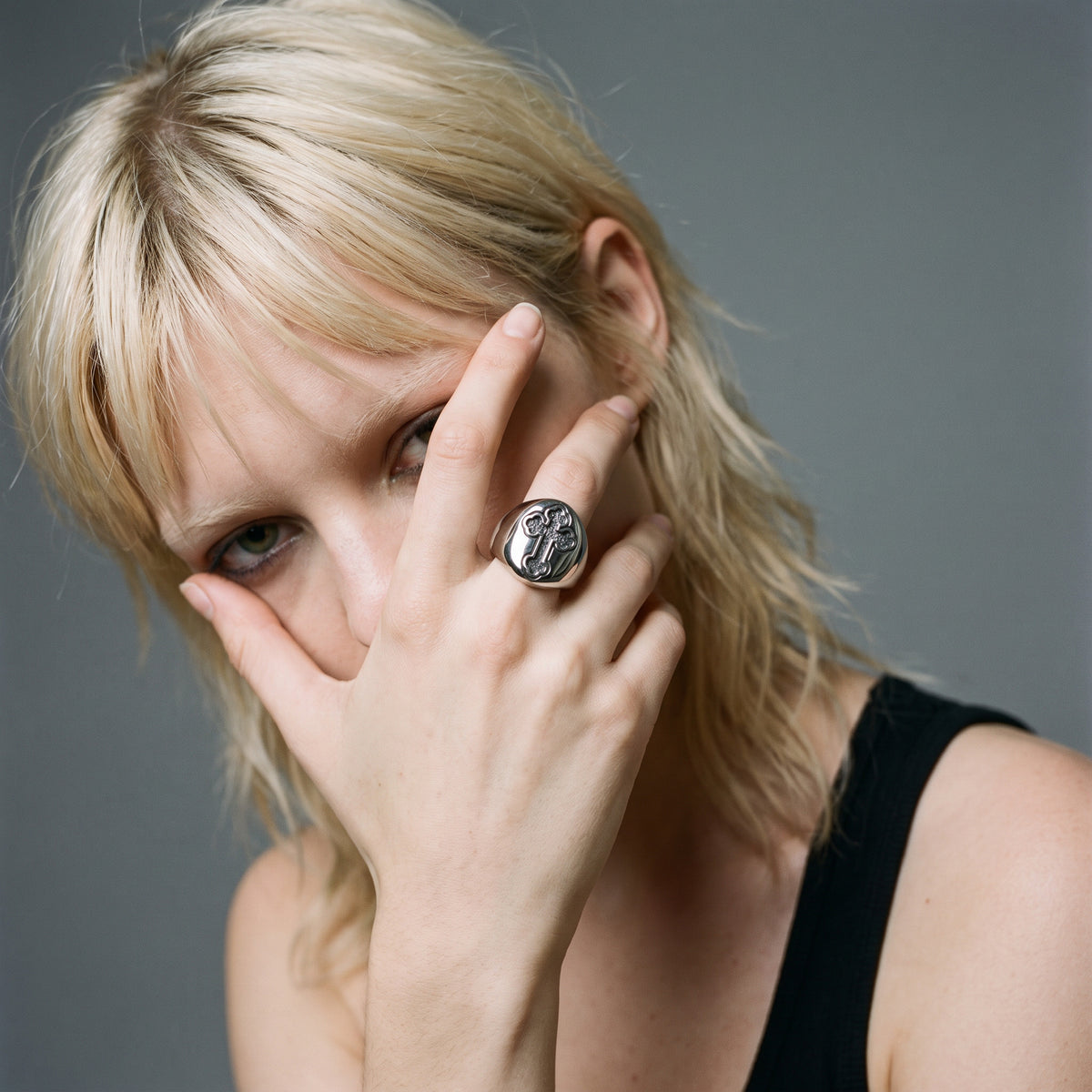 Blonde model with her hand over half her face, wearing the Reliquary Cross Amulet Ring on her index finger, vintage film look