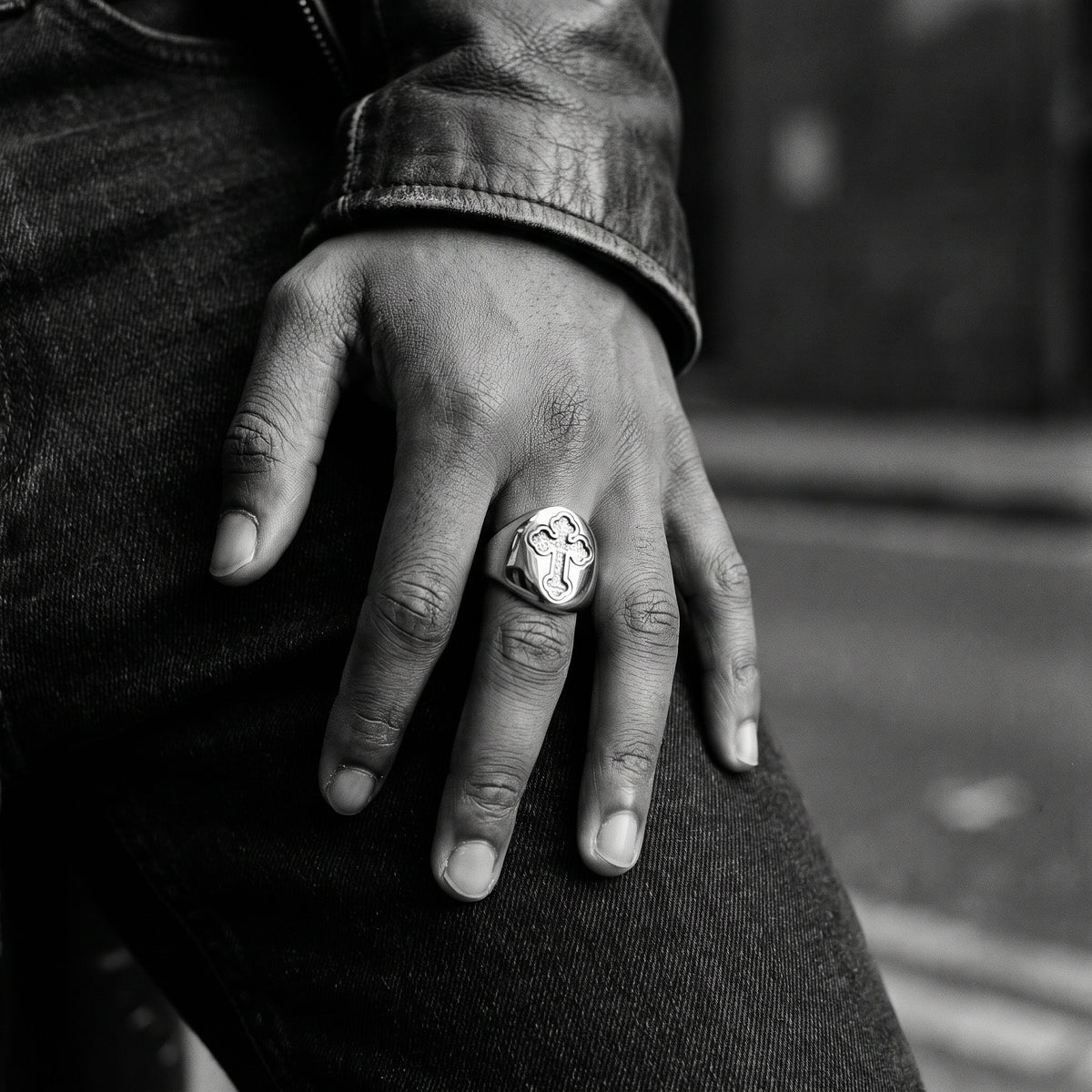 Black and white film photo of a young man's hand resting on dark denim, wearing the Reliquary Cross Amulet Ring