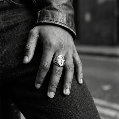 Black and white film photo of a young man's hand resting on dark denim, wearing the Reliquary Cross Amulet Ring