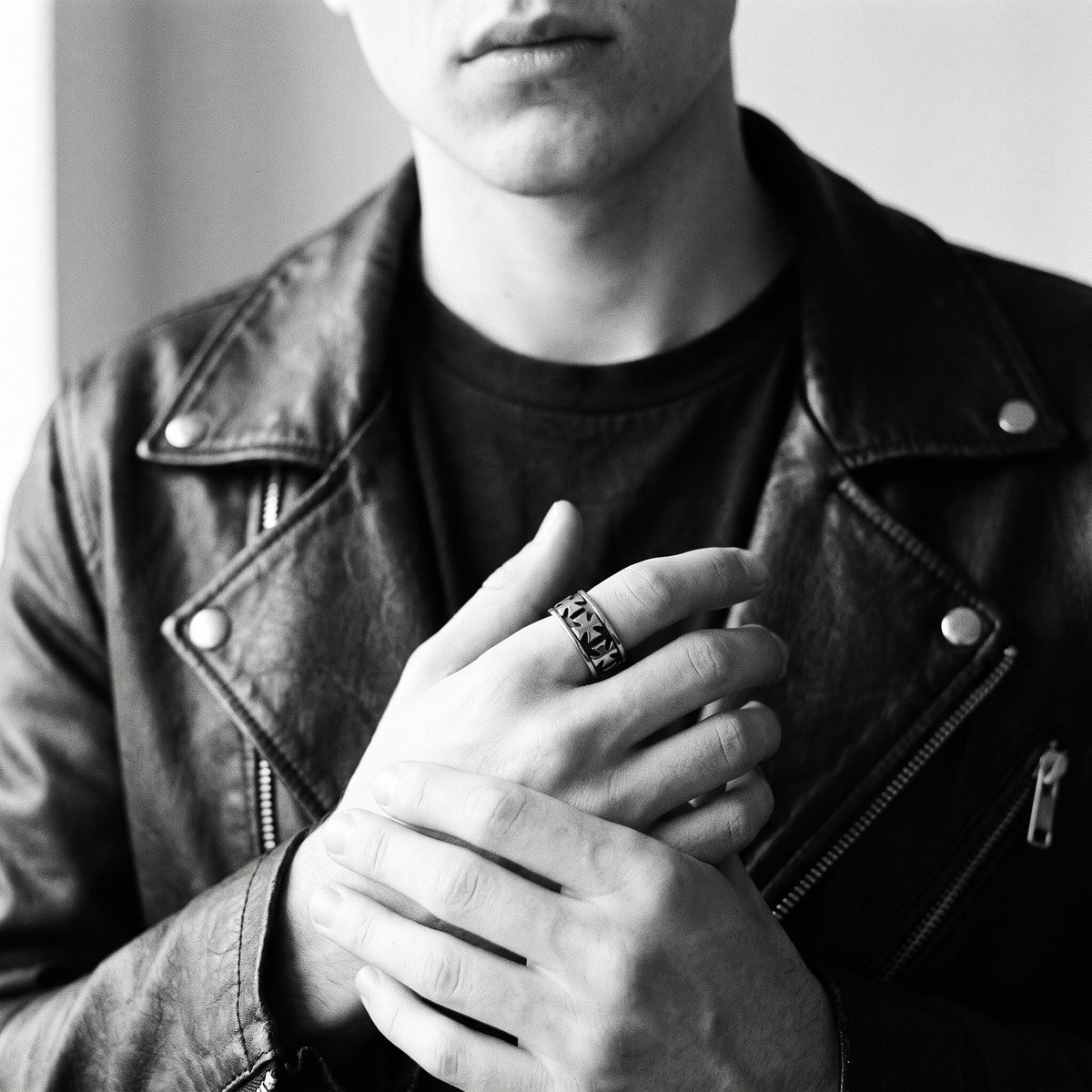 Young man's clasped hands in a black leather jacket wearing the Sacrament cross band ring, black and white 35mm film