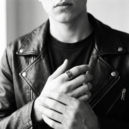Young man's clasped hands in a black leather jacket wearing the Sacrament cross band ring, black and white 35mm film