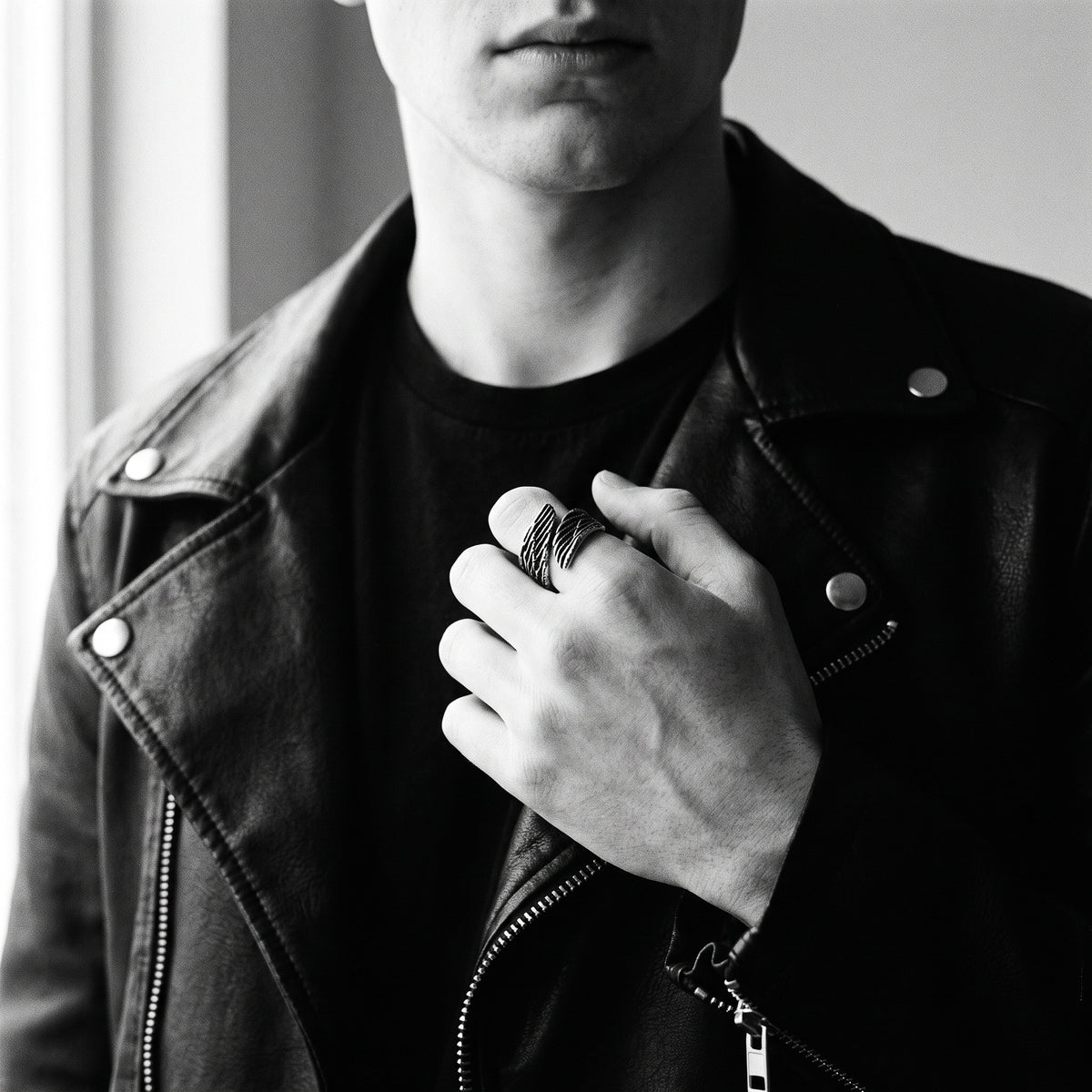 Young man's hand in a black leather jacket wearing the Seraph winged open ring, black and white 35mm film