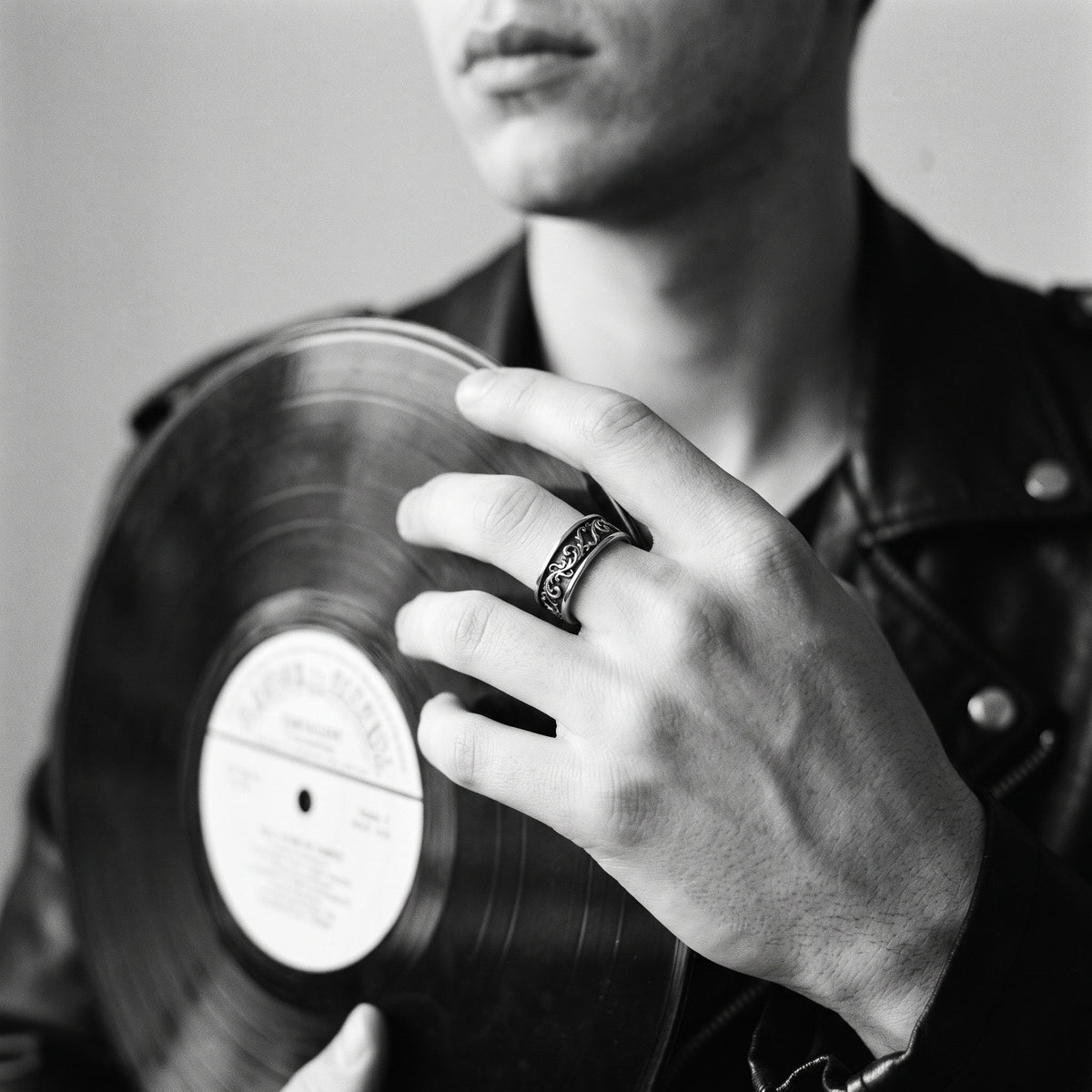 Black and white photo of a hand holding a vinyl record wearing the Skald Viking scrollwork ring