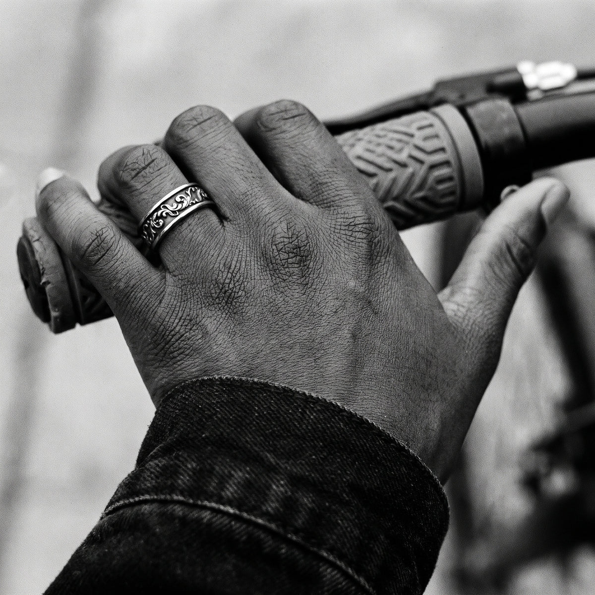 Black and white photo of a hand on a bicycle handlebar wearing the Skald Viking scrollwork ring