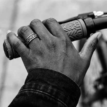 Black and white photo of a hand on a bicycle handlebar wearing the Skald Viking scrollwork ring