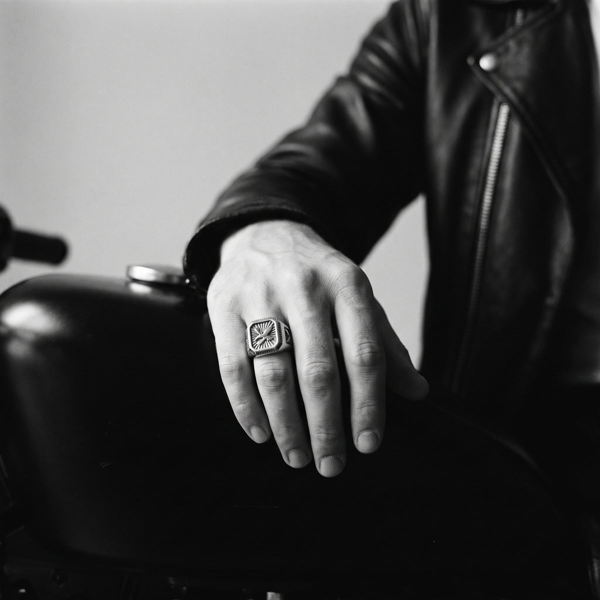 Black and white photo of a hand resting on a motorcycle fuel tank wearing the Talon winged eagle signet ring