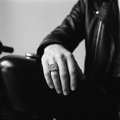 Black and white photo of a hand resting on a motorcycle fuel tank wearing the Talon winged eagle signet ring