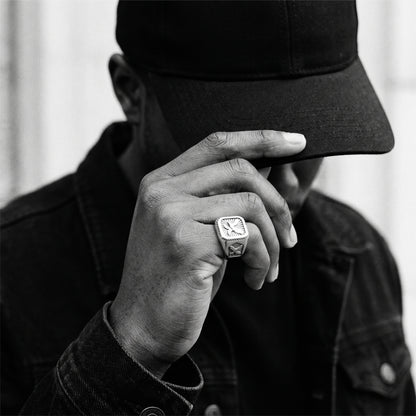 Black and white photo of a hand lifting the brim of a black cap wearing the Talon winged eagle signet ring