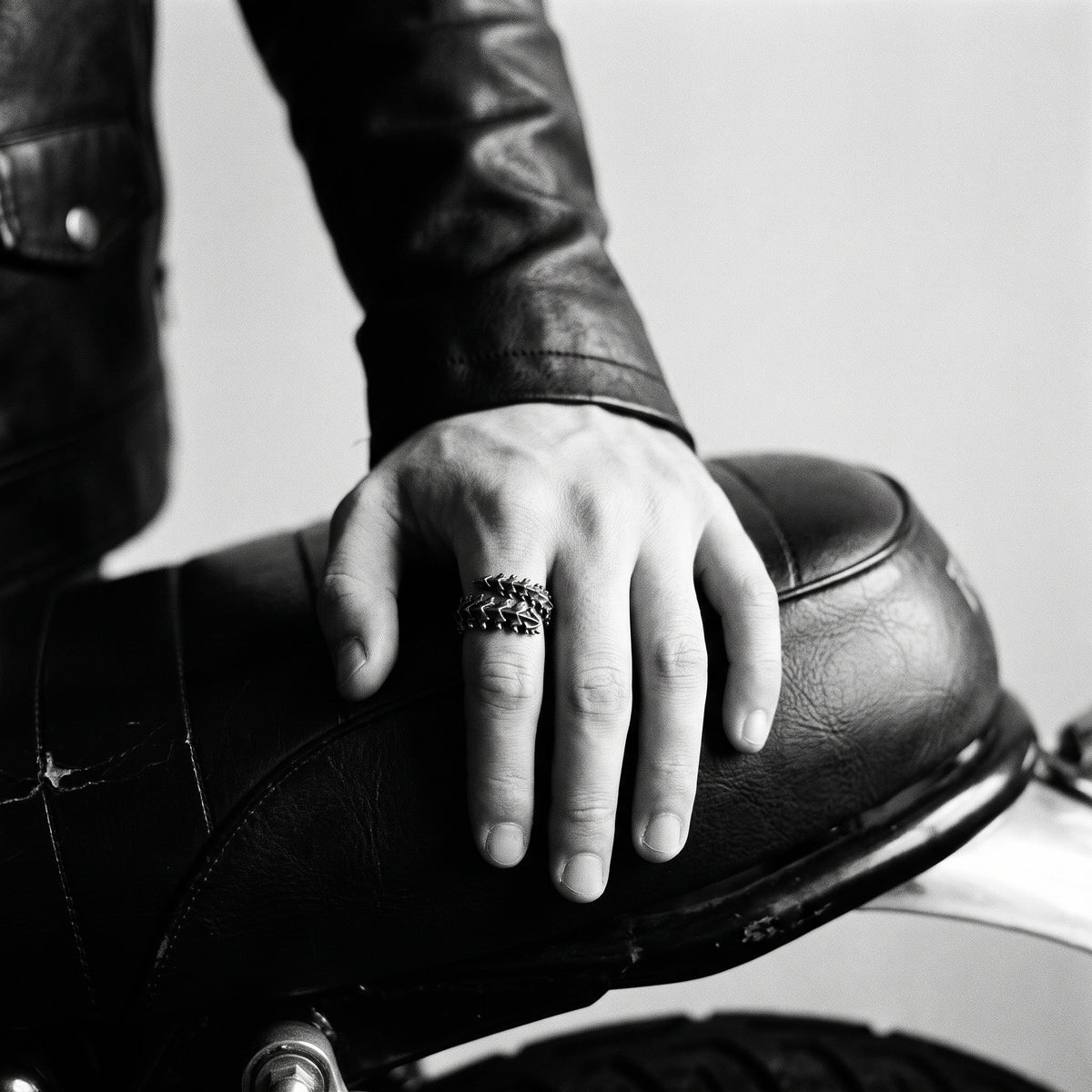 Black and white photo of a hand resting on a leather motorcycle seat wearing the Vertebra dragon bone ring
