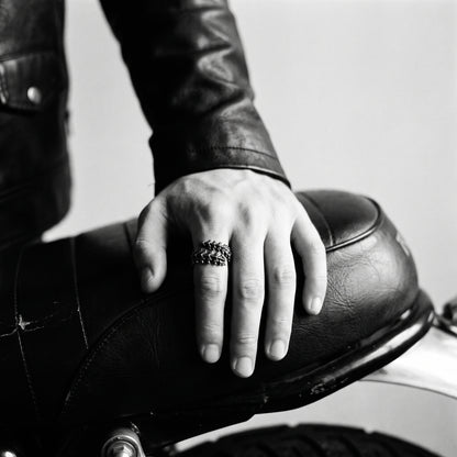 Black and white photo of a hand resting on a leather motorcycle seat wearing the Vertebra dragon bone ring