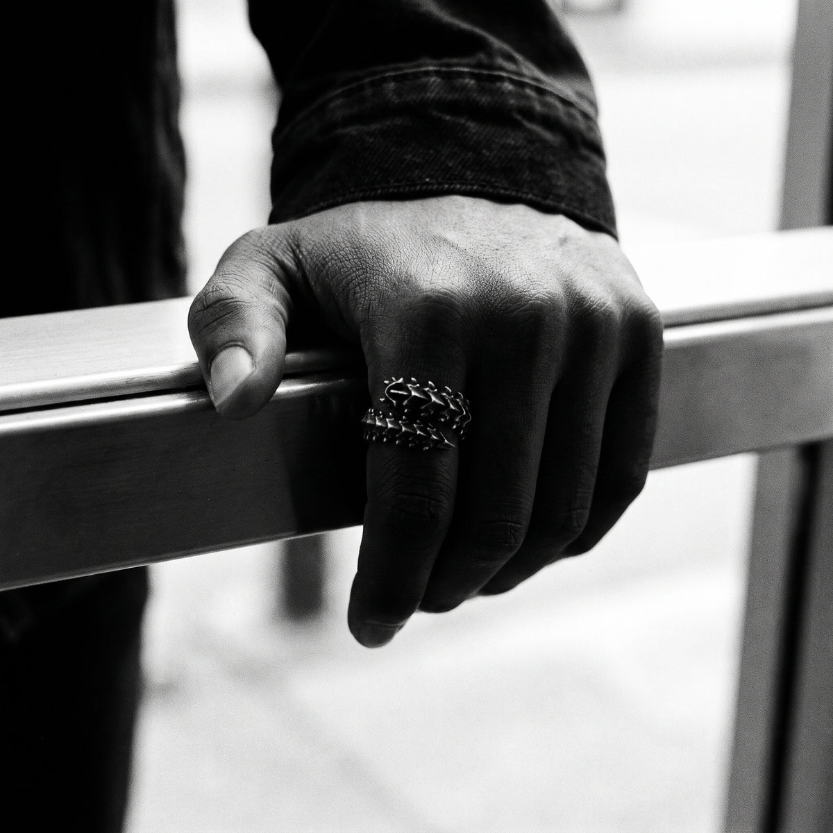 Black and white photo of a hand gripping a metal door push bar wearing the Vertebra dragon bone ring