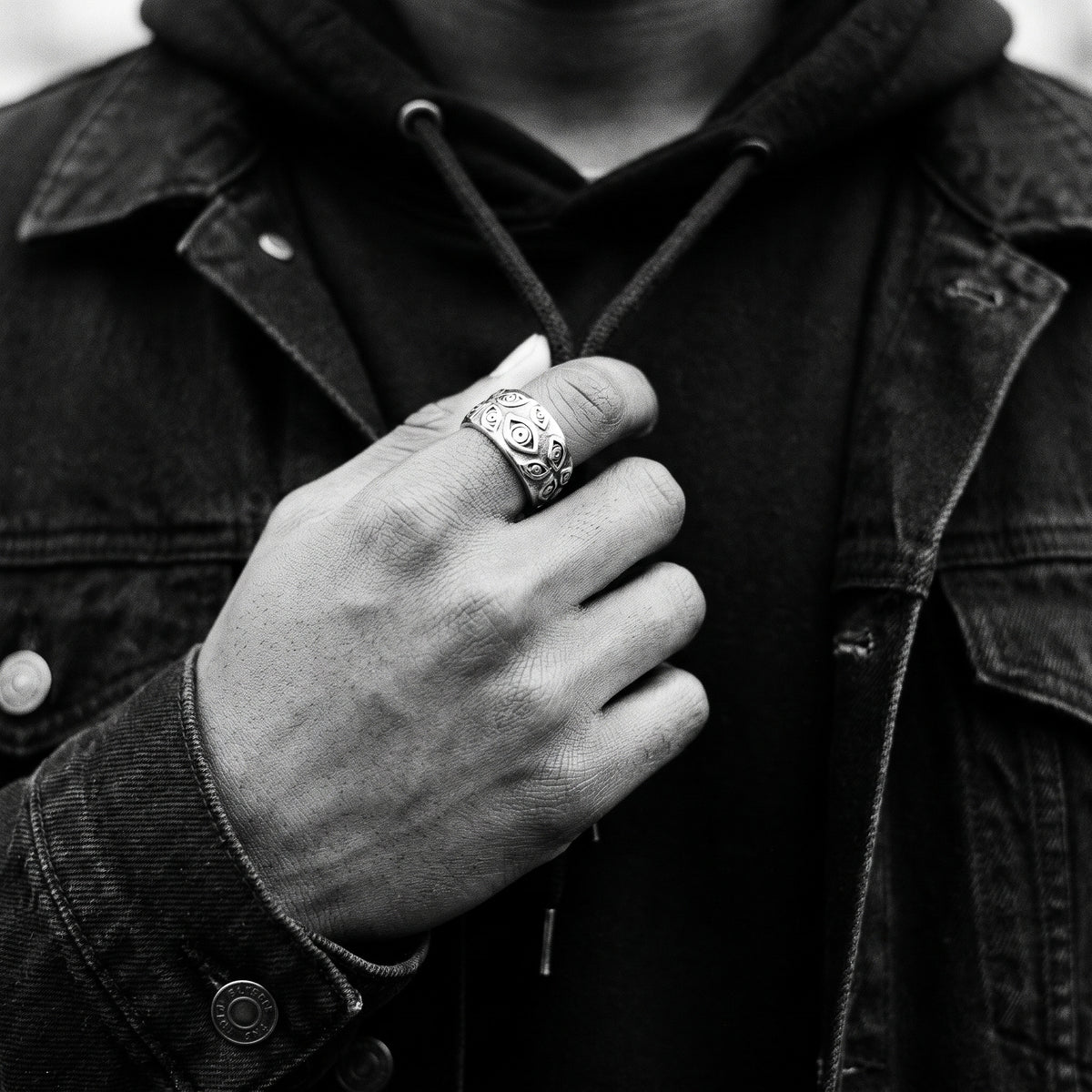 Man's hand on a hoodie drawstring wearing the Watcher eye ring, black and white film photo