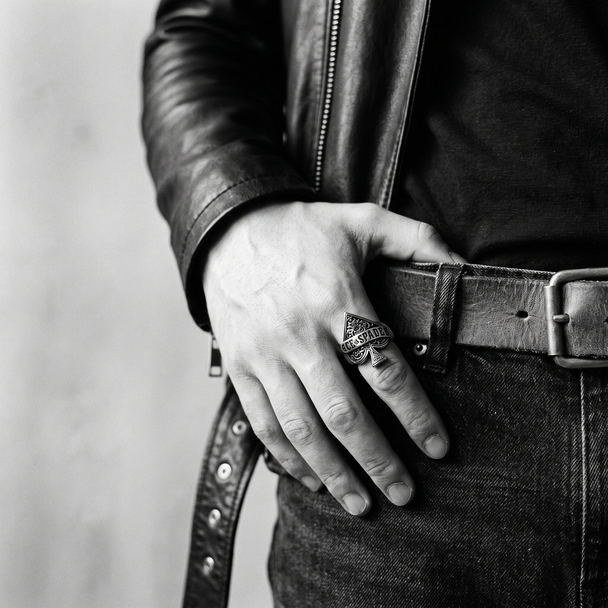 Young man's hand in a black leather jacket, thumb in belt, wearing the Wildcard ace of spades ring, black and white 35mm film