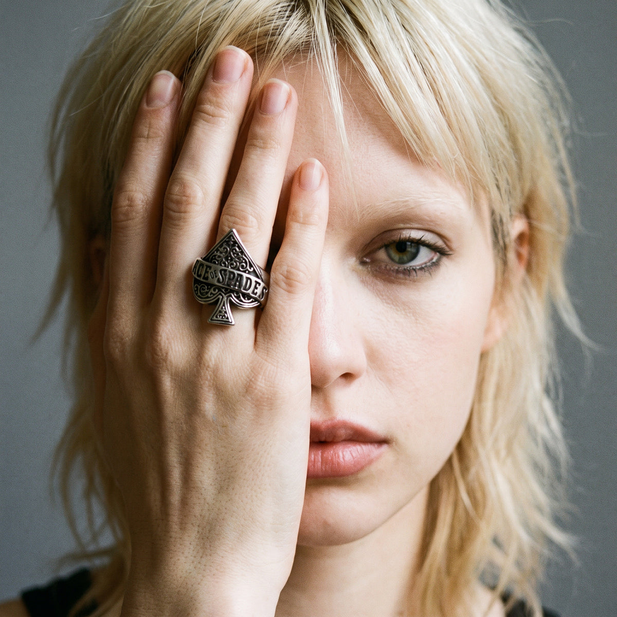 Blonde model with her hand over her face wearing the Wildcard ace of spades ring, vintage film photo