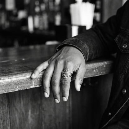 Man's hand resting on a wooden bar counter wearing the Wildcard ace of spades ring, black and white film photo